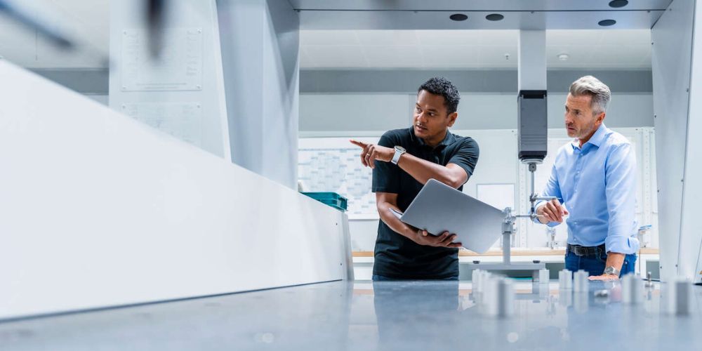 Engineer with laptop pointing by businessman at factory